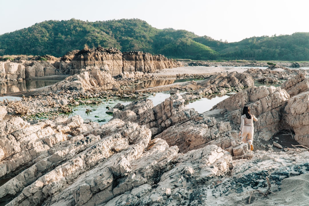 a woman standing on a rocky beach next to a body of water